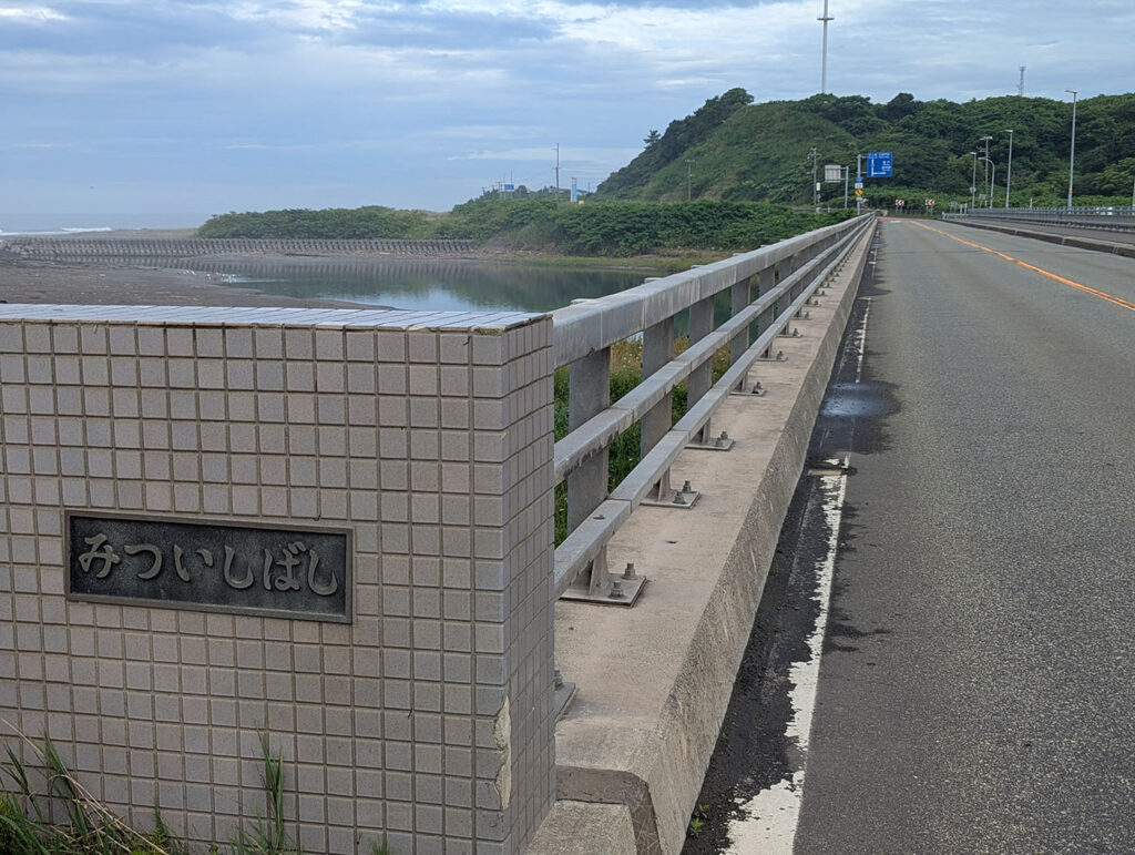 北海道新ひだか町の三石橋の欄干と橋名プレート。道路と川、遠景に緑の丘が広がる。
