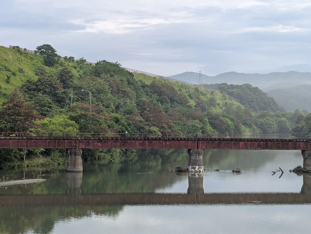 三石橋から眺めた廃線となった旧鉄道橋と川、背景に広がる緑と山並み。