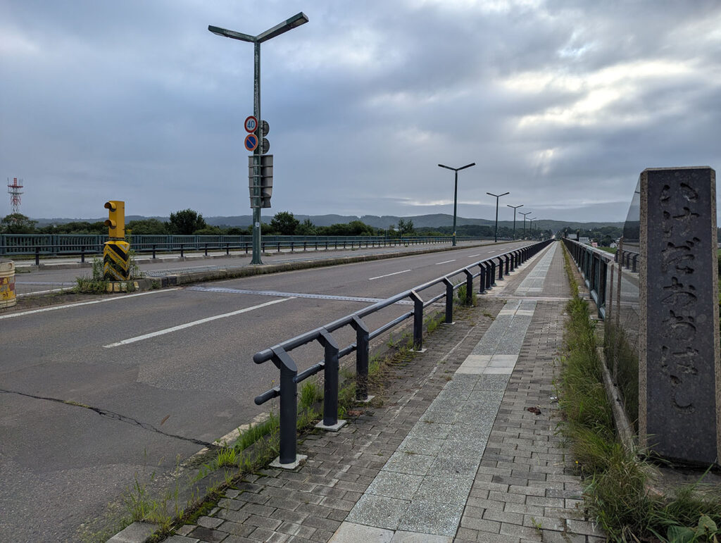 曇り空の下、池田大橋の橋名碑と並行して延びる車道と歩道