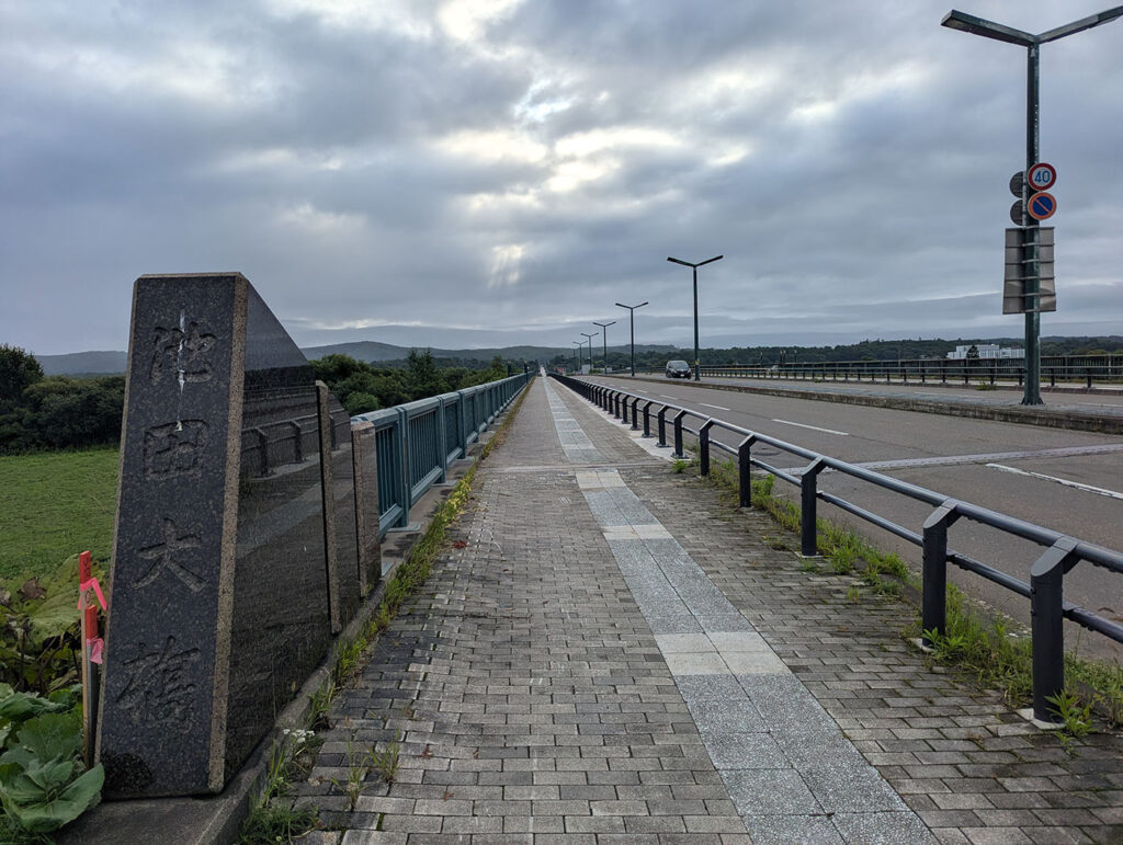 曇り空の下、池田大橋の橋名碑とまっすぐ延びる歩道と車道