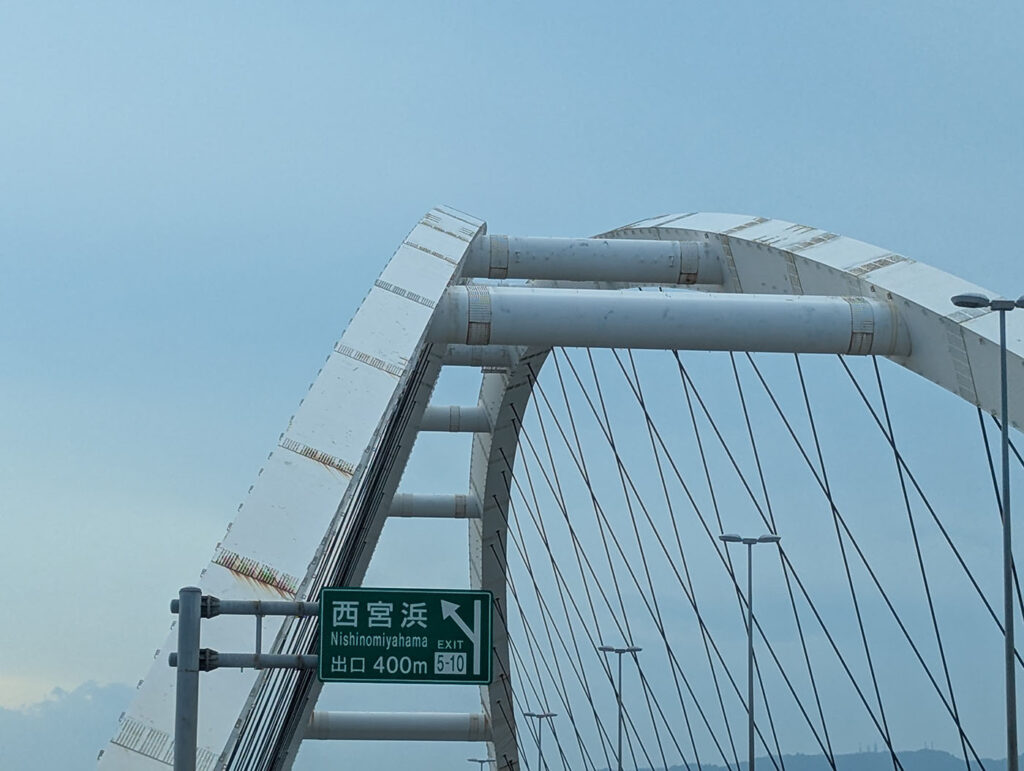 白いアーチが美しい東浜大橋。斜めに伸びる無数のケーブルが、空に繊細なラインを描いている。手前には「西宮浜出口」の標識が見える。
