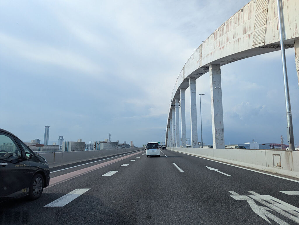 大阪・南港大橋を走行する車列と、白いアーチ構造が空へ伸びる風景