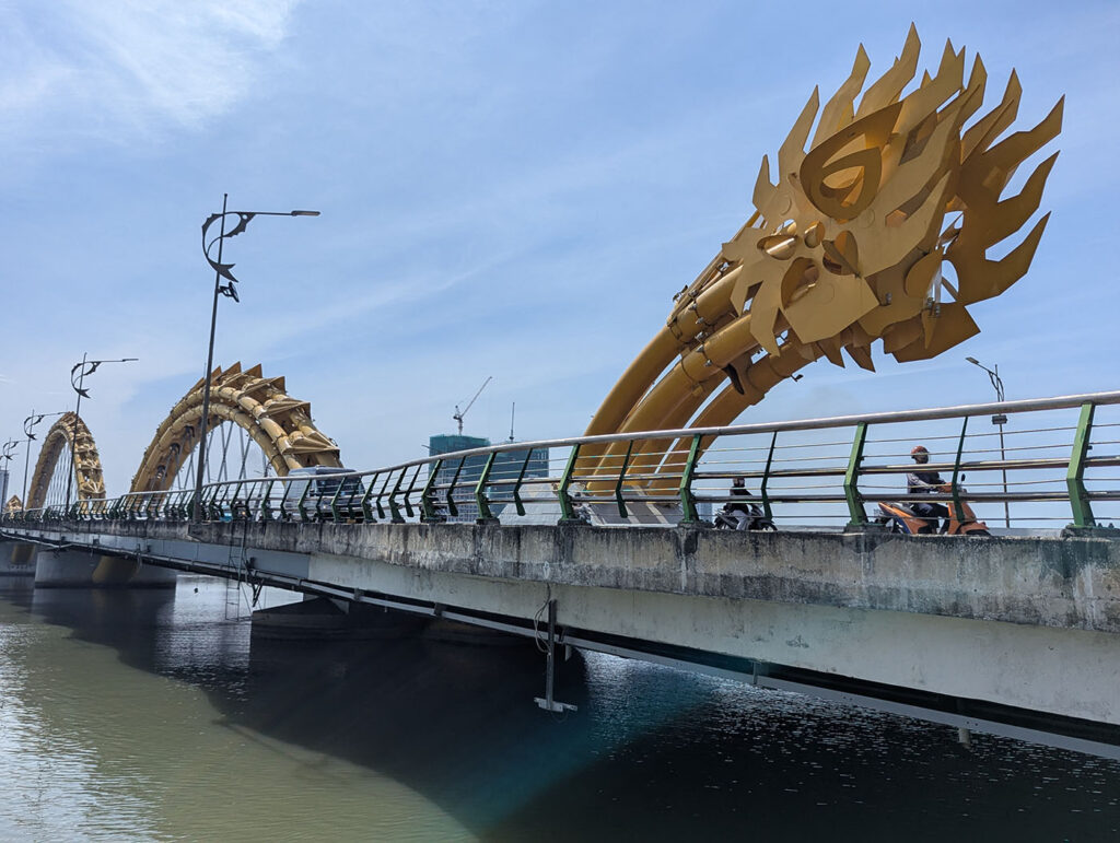 バイクが行き交うダナン・ドラゴンブリッジの全景と黄金の龍の頭部